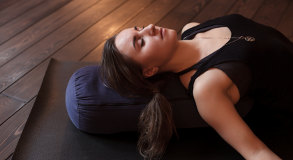 Woman resting after a yoga class in Corpse Pose or Savasana with bolster for spine comfort