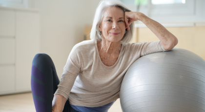 Smiling elderly woman resting on a swiss ball at home