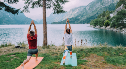Fitness lifestyle concept - sportive couple making yoga exercises sitting on mats outdoors near lake
