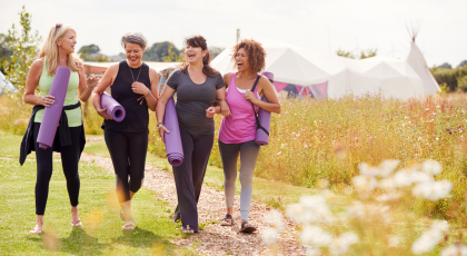 Group Of Mature Female Friends On Outdoor Yoga Retreat Walking Along Path Through Campsite.