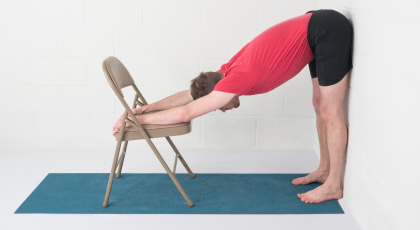 Uttanasana or Standing forward Fold Pose variation with the support of the wall and a chair. 