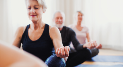 Group of active senior people doing yoga exercise in community center club.