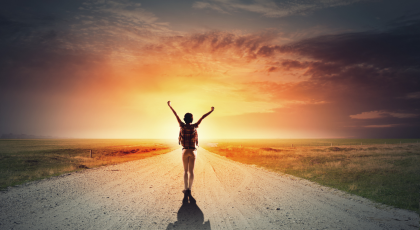 Rear view of girl with hands up facing sunrise.