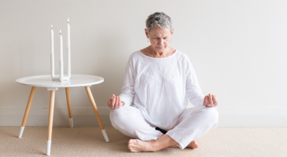 woman in white sitting in yoga meditation position with candles against neutral wall background