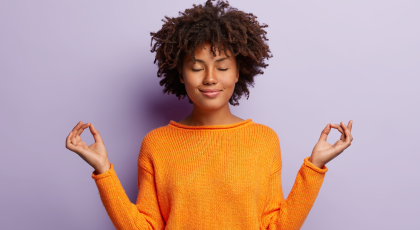 woman in orange clothes meditates indoor, holds hands in mudra gesture