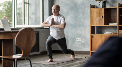Senior hispanic man standing in warrior yoga pose variation practicing in living room alone