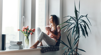 Thoughtful young woman in cozy pajamas looking through the window while resting at home