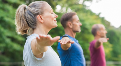 Group of senior people with closed eyes stretching arms at park. Happy mature people doing yoga