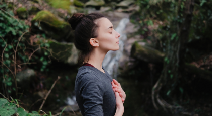 woman near a waterfall, practicing breathing and yogic affirmation of going with the flow of Life