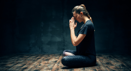 Rear view of young woman practicing yoga's Lotus Pose with namaste hands in dark room