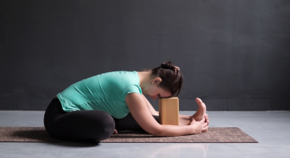 woman practicing janu sirsasana yoga pose with block under her forehead