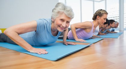 An older woman in a yoga class in Cobra Pose (Bhujangasana) practicing yoga for osteoporosis