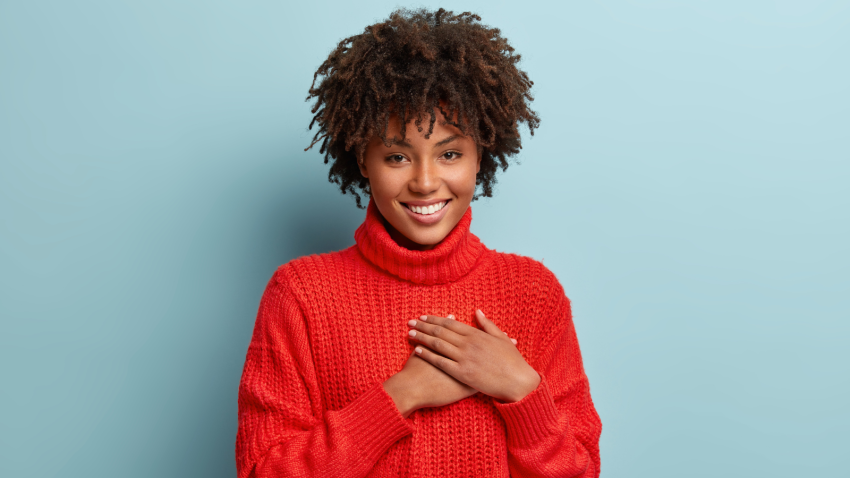 How to practice gratitude to fortify resilience. Photo of emotional female touching her heart with both palms, demonstrates thankful gesture.