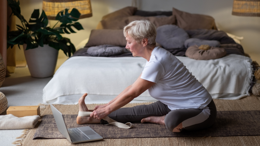 Senior woman practicing yoga pose Janu Sirsasana or Head-to-Knee Forward Bend Pose, working out at h