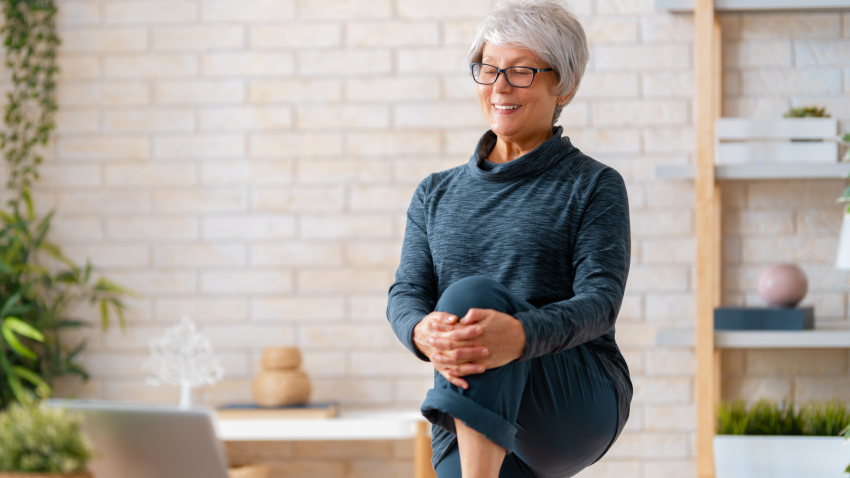 Senior woman in activewear watching online courses on laptop while practicing strengthening poses at