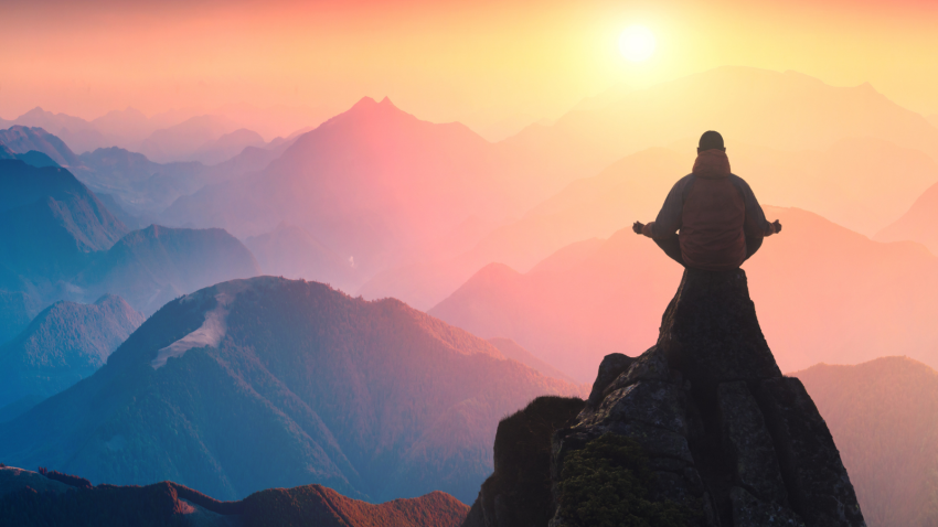 A person practicing meditation, reflecting on the Yamas, or ethical rules within yogic philosophy. A silhouette of a person meditating on top of a mountain above a misty valley.