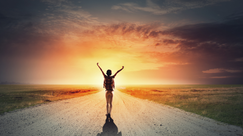 A woman raising her arms in joy while walking on a road towards a sunset, depicting the feeling of self-healing. woman raising her arms in joy walking on road towards a sunset, depicting feeling of self-healing