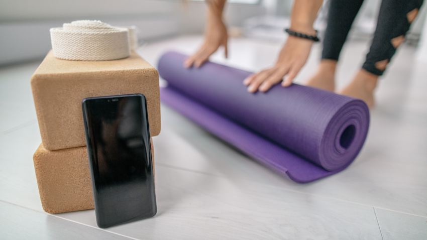 Cells phones and yoga to allow or not to allow? Student rolling out mat getting ready for yoga class with mobile smartphone close by
