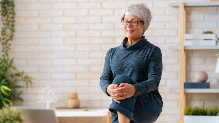 Exercising and movement can help alleviate pain. Senior woman in activewear watching online courses on laptop while exercising at home.