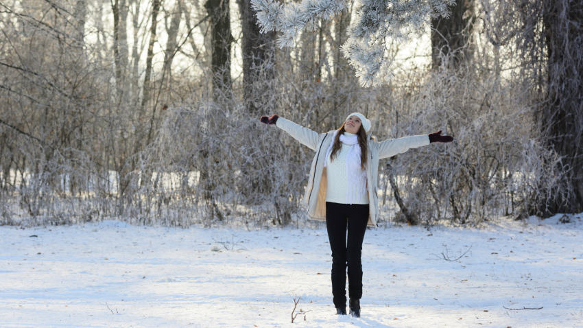 How to be outside in the snow and enjoying the moment. Smiling young woman with arms out to the side, representing feeling free