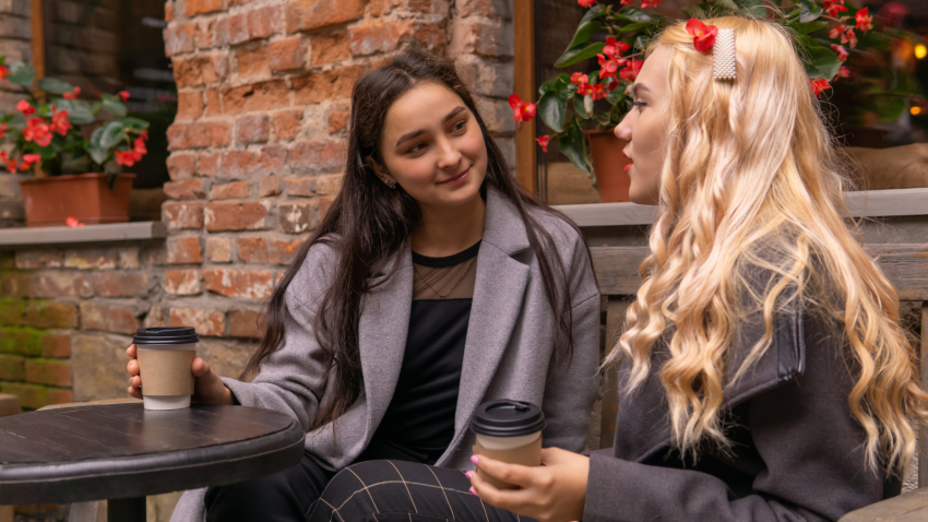 How to listen carefully with eye contact and interest. Girl listens carefully to her friend talking about something on a bench with coffee outdoors