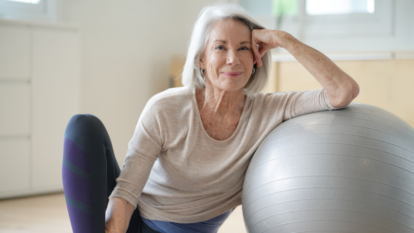Smiling elderly woman resting on a swiss ball at home