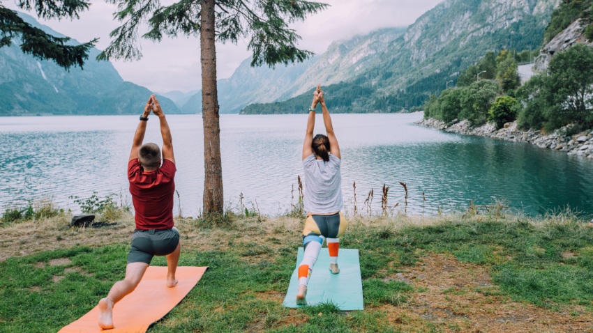 How to replenish with exercise and nature for greater resilience Fitness lifestyle concept - sportive couple making yoga exercises sitting on mats outdoors near lake