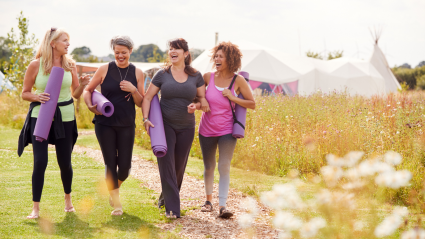 How to spend more time in nature and with friends. Group Of Mature Female Friends On Outdoor Yoga Retreat Walking Along Path Through Campsite.