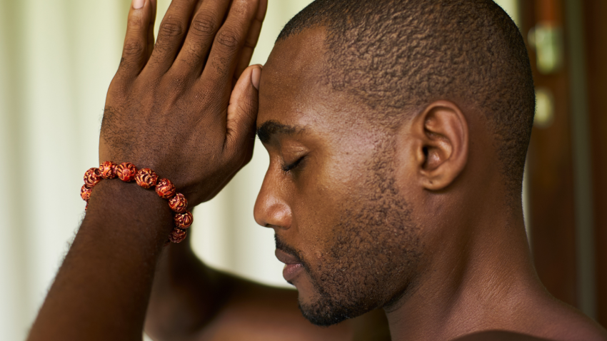 Image depicts man with hands in mudra and spiritual wellbeing. Portrait of an African American male with praying hands or Anjali Mudra to his forehead