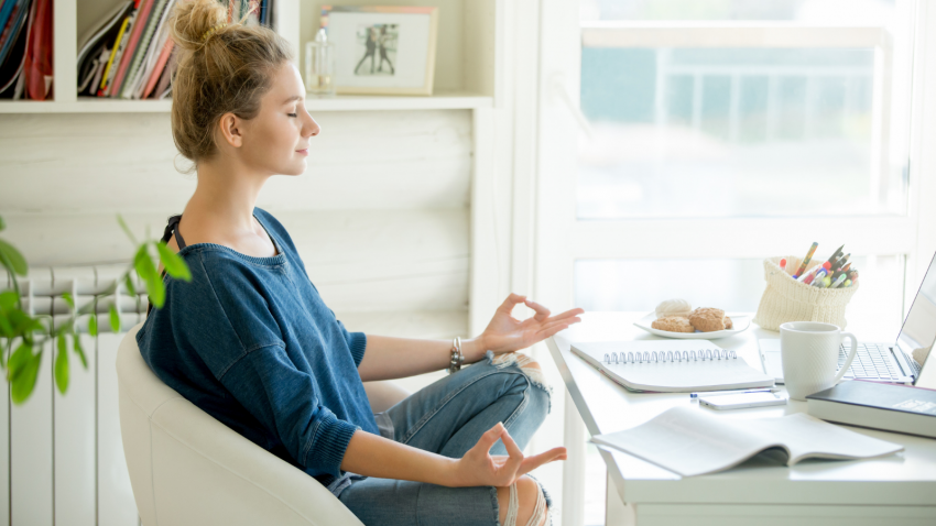 One way to practice mindfulness-- pausing to reflect attractive woman in a chair seating in Lotus pose in front of table with laptop