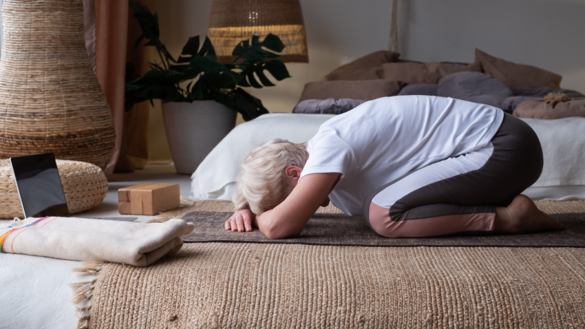 Yoga Poses that might work well to reduce symptoms of Long COVID Senior woman working out indoors, doing forward bend yoga exercise Balasana, Child Pose.