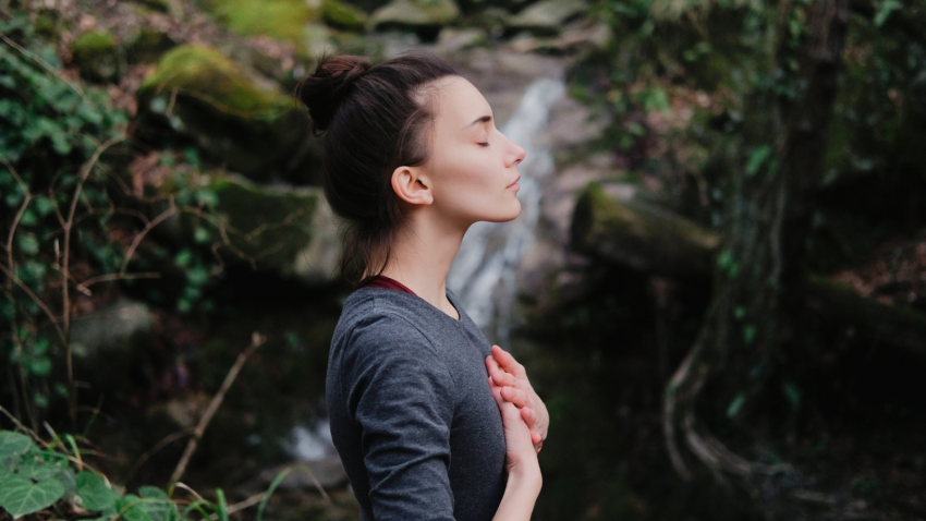 Young woman by a waterfall practicing Swadhisthana Chakra Mudra of going with the flow of life woman near a waterfall, practicing breathing and yogic affirmation of going with the flow of Life