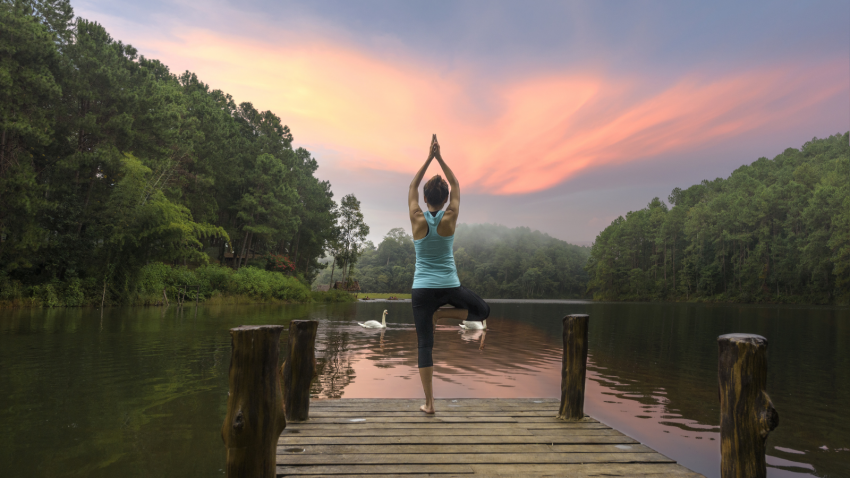 Yoga student practicing yoga at lake surrounded by water, earth and sky representing ayurvedic elements woman practicing yoga at lake surrounded by water, earth and sky representing ayurvedic elements