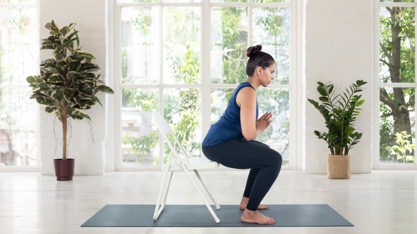 Woman practicing Chair Pose Utkatasana on a folding chair. Woman practicing Chair Pose Utkatasana on a folding chair.