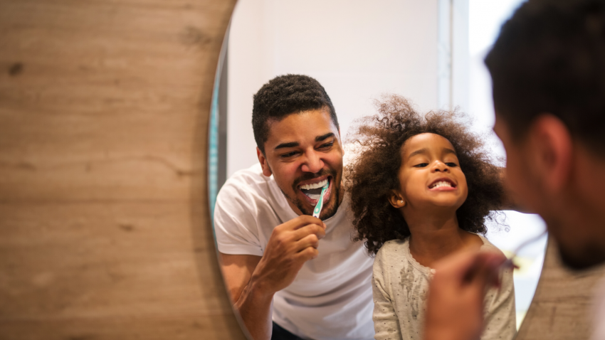 Father and daughter happily brushing teeth together in the mirror. Father and daughter happily brushing teeth together in the mirror.