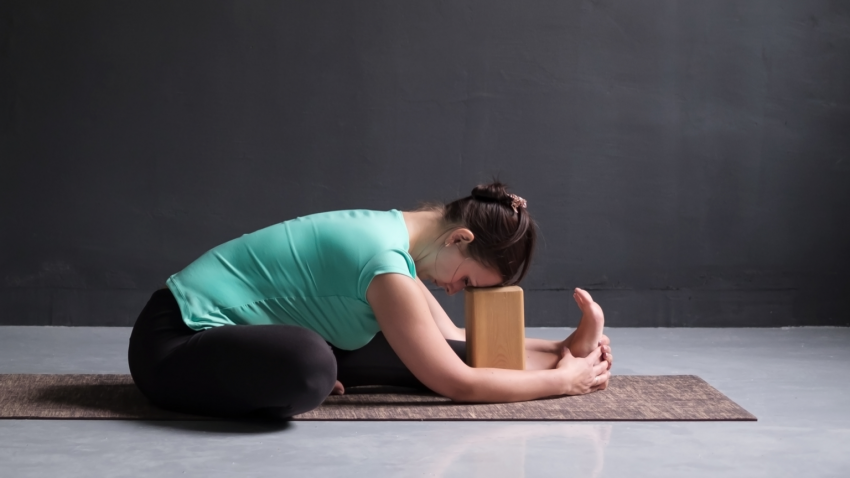 woman practicing janu sirsasana yoga pose with block under her forehead