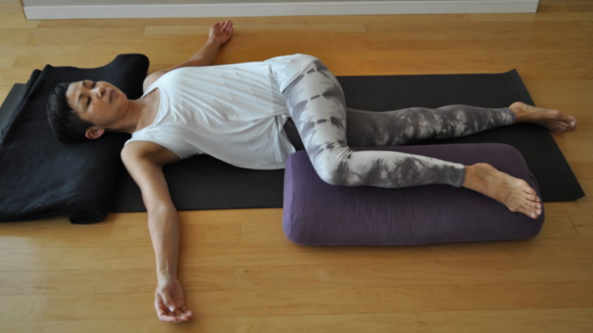 How to practice Supported Supine Twist (Jathara Parivartanasana). Student practicing a supported (by bolster) restorative twist for greater comfort and ease