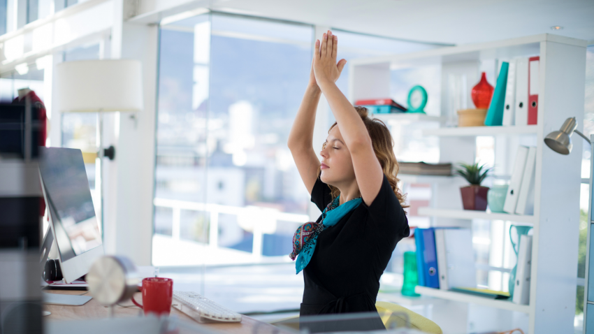 Woman doing yoga poses at desk to relieve strain from sitting Woman doing yoga poses at desk to relieve strain from sitting