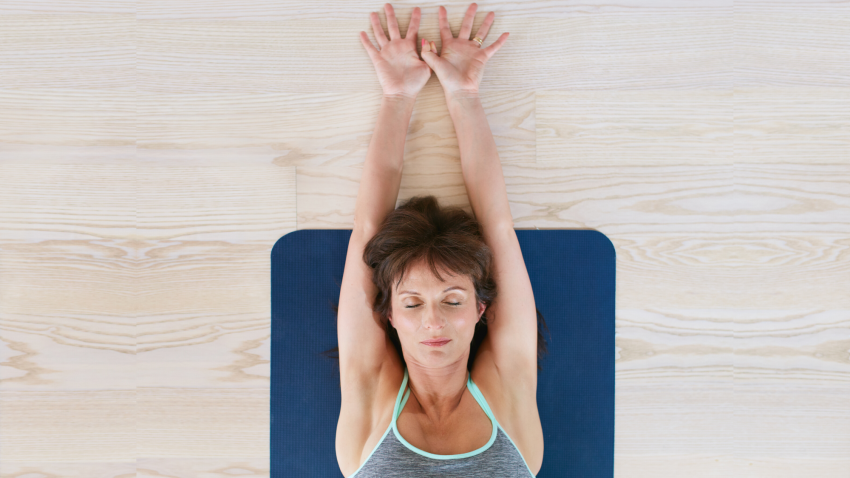 Woman stretching her arms overhead while lying on yoga mat. 